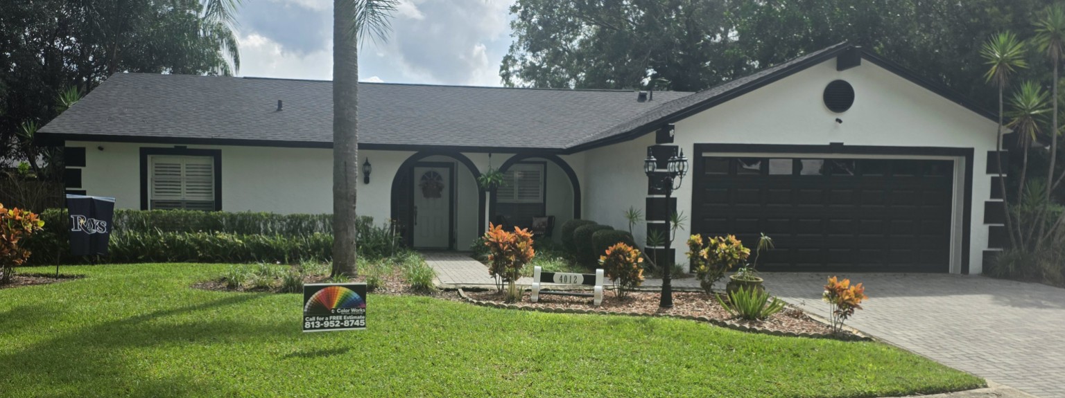 After: the home with a fresh white exterior, dark garage door, and Color Works yard sign